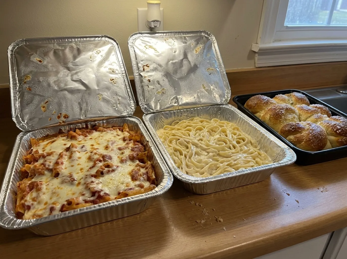 Labeled Italian catering trays of pasta, salad and garlic rolls set up for an office lunch near Avalon