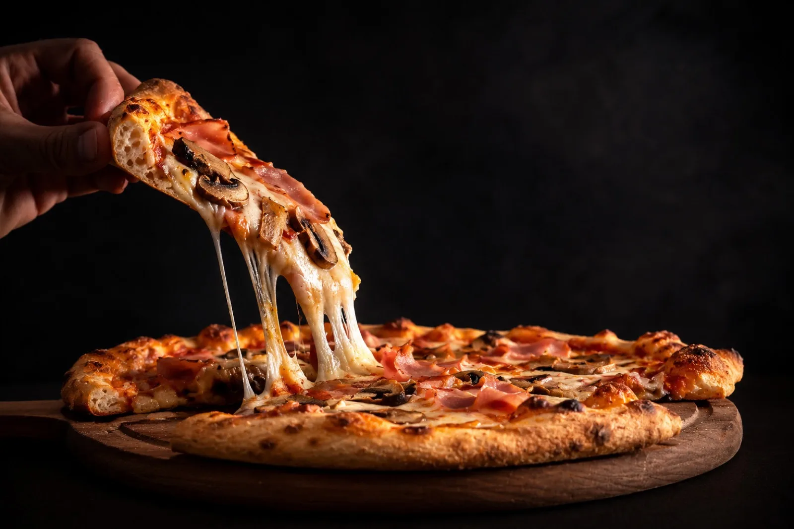 A hand pulling a slice of hot delivery pizza with a long cheese stretch