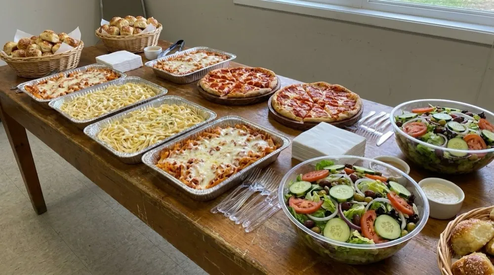 Vito's Italian catering buffet — baskets of garlic knots, foil trays of pasta, fresh pizzas and garden salads spread across a table